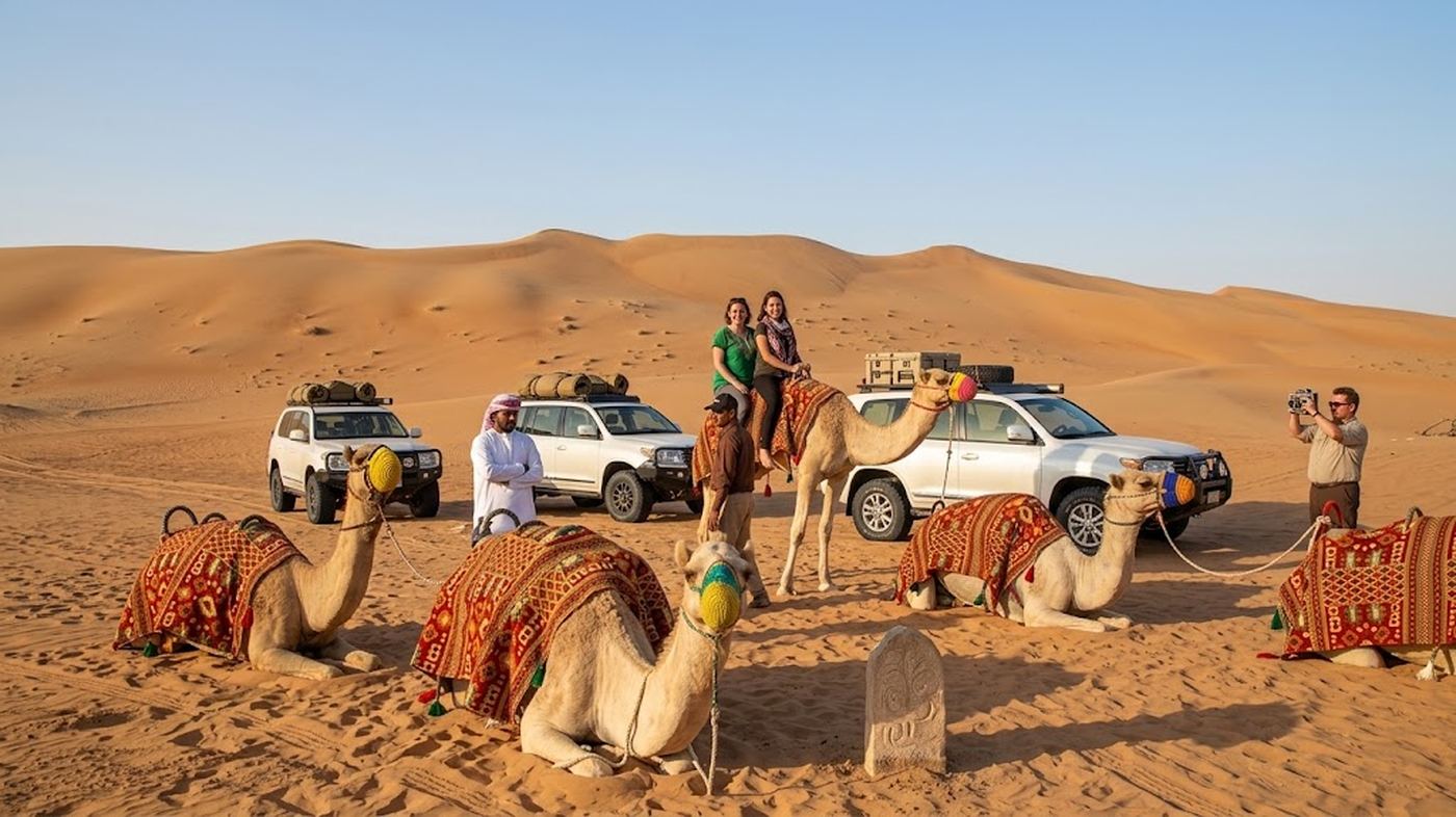 Camel caravan riding through the dunes at sunset